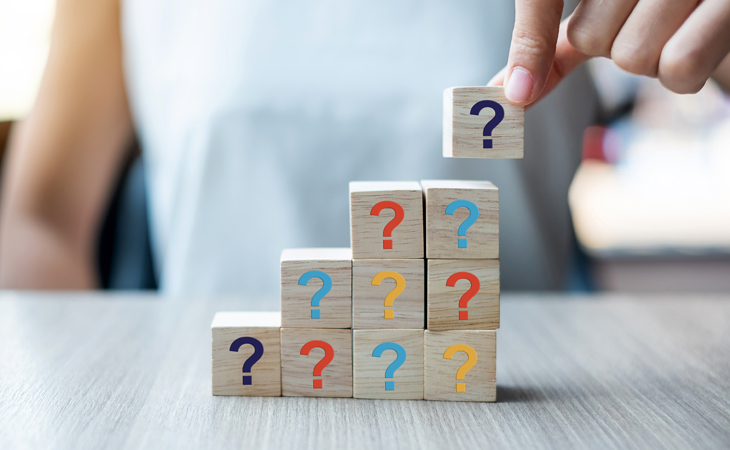 Person stacking wooden building blocks with question marks on the face