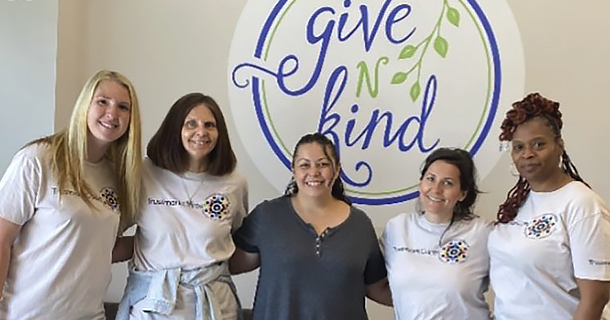 Smiling group of employees in front of Give N Kind sign